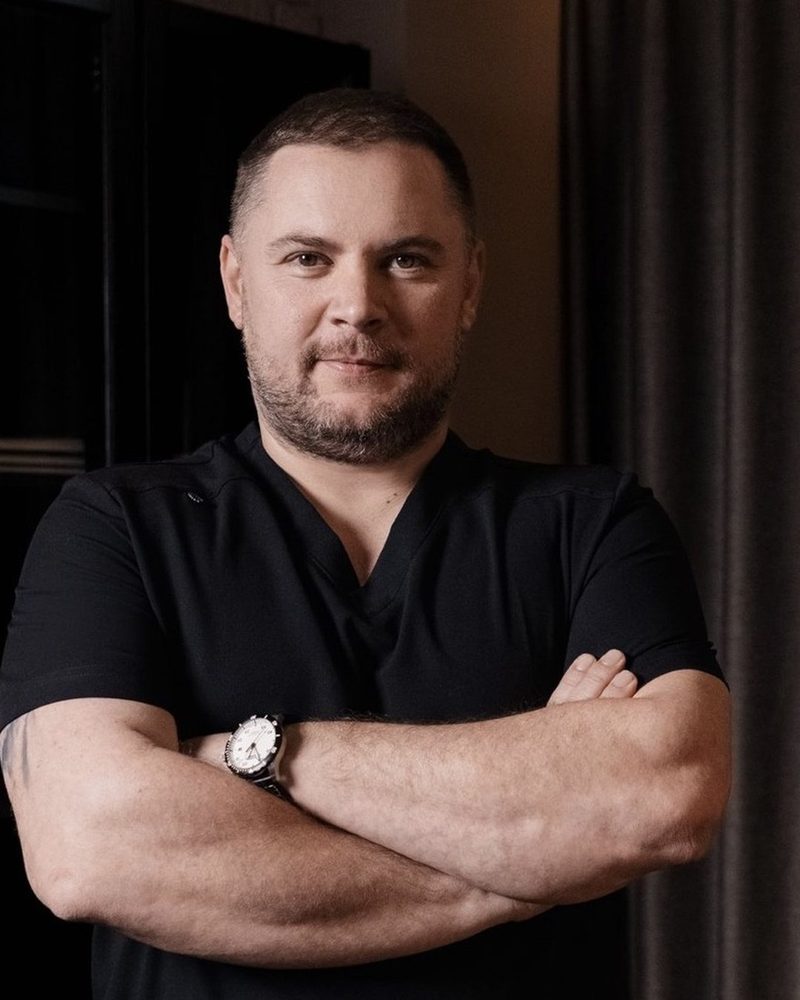 Лікар акушер-гінеколог у чорній медичній формі, руки схрещені